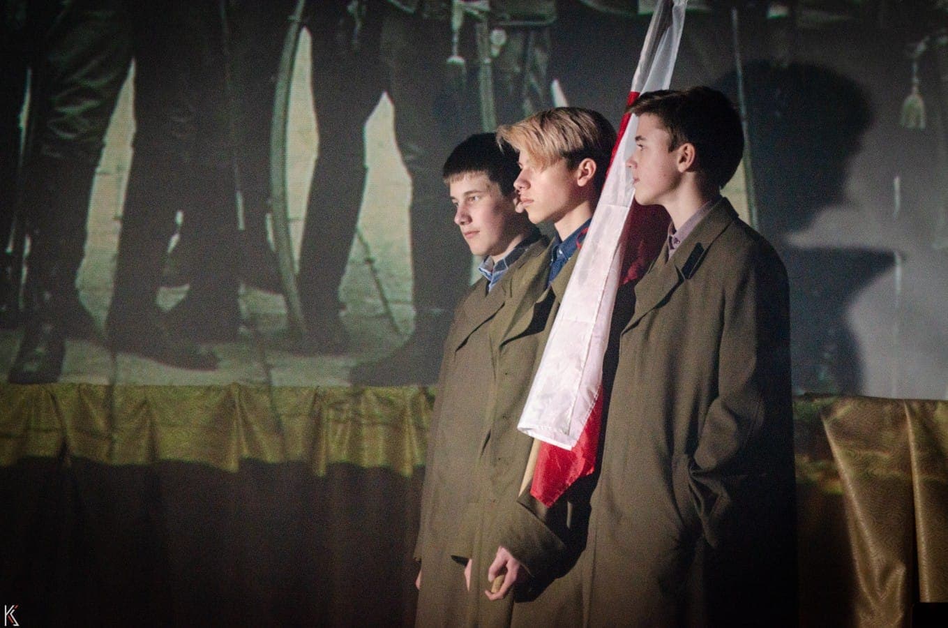 Учні в шинелях із біло-червоним прапором у шкільній історичній виставі